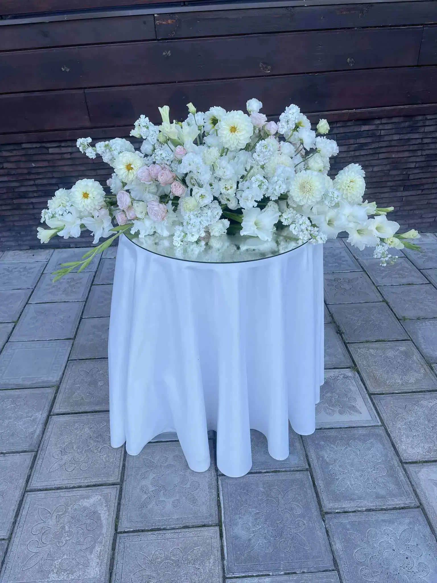 White dahlias, stock, and gladiolus with blush spray roses on a mirrored table